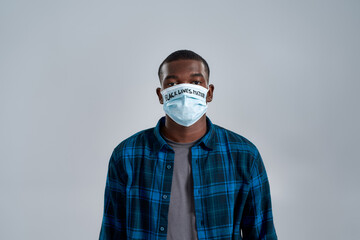 Portrait of young african american man wearing protective mask with inscription BLM, looking at camera, posing isolated over gray background