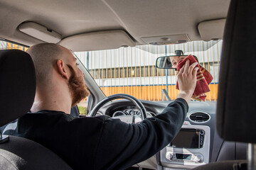 Hombre joven en el asiento del conductor limpiando el espejo retrovisor con un paño