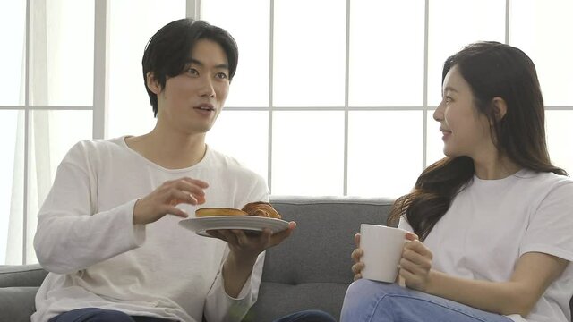 Loving couple sitting on sofa at home. Man and woman relaxing on couch with smartphone in living room.