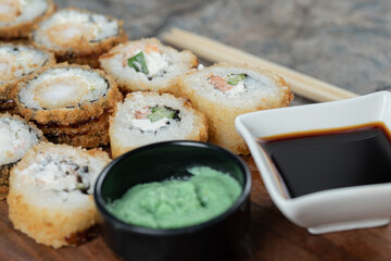 Fried hot sushi rolls on a wooden board with wasabi and soy sauce