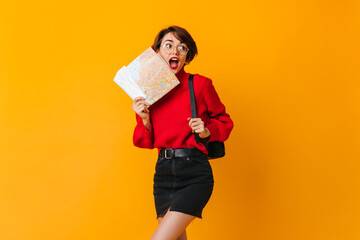 Blissful brunette woman holding map. Emotional girl with backpack standing on yellow background.