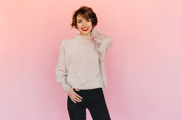 Good-looking young woman in sweater looking at camera. Studio shot of appealing short-haired girl with red lips.