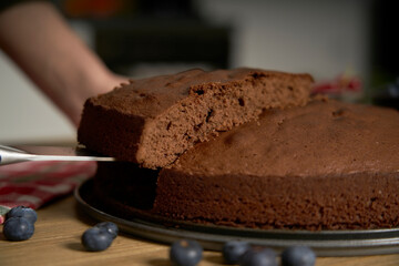 Woman with a passion for cooking cuts a slice of handmade chocolate cake in her home kitchen.