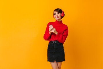 Pensive girl in black skirt holding smartphone. Studio shot of blissful short-haired lady in headphones.