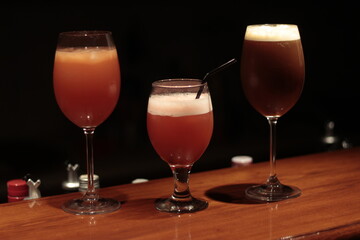 Three cocktail drinks on a bar, dark background