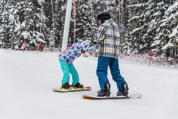 The father teaches his daughter to snowboard