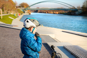 Ein Junge mit Fahrrad, Helm, Handschuhe am Wasserkanal, Fluss im Frühling 