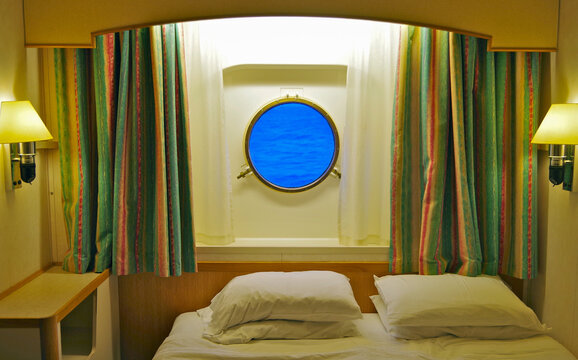 Comfortable oceanview or outside stateroom cabin suite with porthole window in dated old fashioned interior design onboard classic cruiseship or cruise ship liner with double bed and pillows