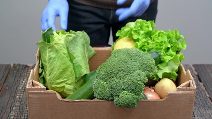 A man puts fresh vegetables in a box with hygienic gloves for donation to the poor and needy. During a pandemic, for delivery.