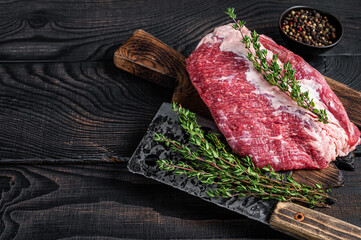 Fresh Raw Round roast beef meat cut on a butcher cutting board with cleaver. Black wooden background. Top view. Copy space