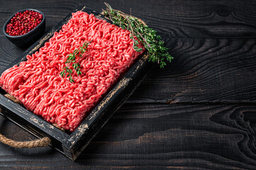 Raw mince ground beef and pork meat in a wooden tray with herbs. Black background. Top view. Copy space