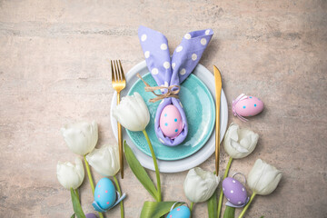 Easter holiday table setting with bunny  from egg on white plate and tulips flowers.  Gray concrete table, top view with copy space for text. Happy Easter background