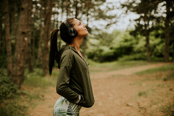 Young beautiful female runner listening to music and taking a break after jogging in a forest