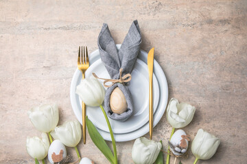 Easter holiday table setting with bunny  from egg on white plate and tulips flowers.  Gray concrete...