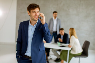 Handsome young business man standing confident in the office and suing mobile phone