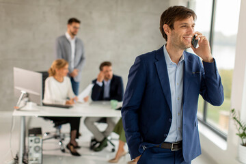 Handsome young business man standing confident in the office and suing mobile phone