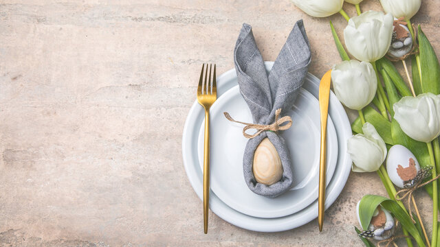 Easter holiday table setting with bunny  from egg on white plate and tulips flowers.  Gray concrete table, top view with copy space for text. Happy Easter background