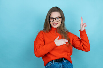 Pretty woman with long hair wearing a casual sweater and glasses over blue background smiling...