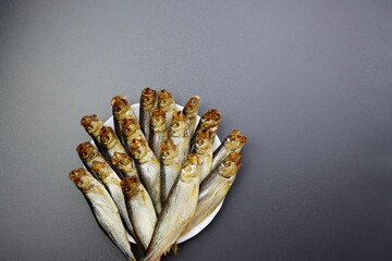 Smoked sprats are stacked on top of each other on a gray background. Smoked fish. 
