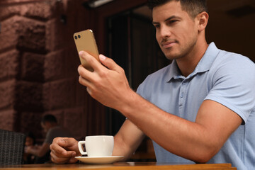 Man unlocking smartphone with facial scanner in outdoor cafe. Biometric verification