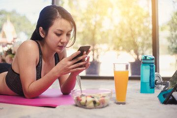 Healthy Asian woman diet eating salad fruit after exercise. Young woman in sportswear and use smartphone with bowl salad fruit.