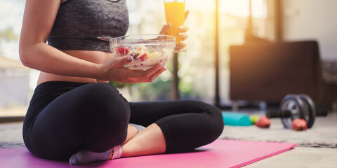 Selective focus hand holding salad fruit  in the bowl. Fitness sport woman in fashion sportswear eating healthy salad fruit bowl. Healthy eating, dieting and exercise  concept.