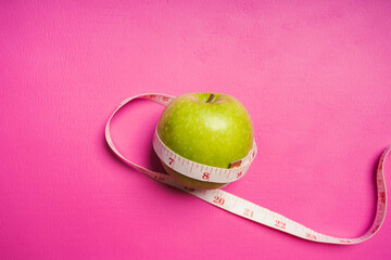 Healthy food fitness, Green apple with salad measure tape on pink yoga mat. Health care, exercise concept.