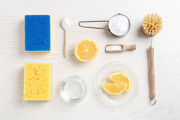 Fototapeta na wymiar Baking soda, vinegar, lemon, cleaning brush and sponges on white wooden table, flat lay