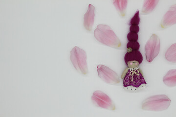 small purple doll, surrounded with pink petals, white background 