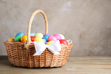 Fototapeta na wymiar Wicker basket with bright painted Easter eggs on wooden table against grey background. Space for text