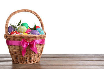 Colorful Easter eggs in wicker basket on wooden table against white background