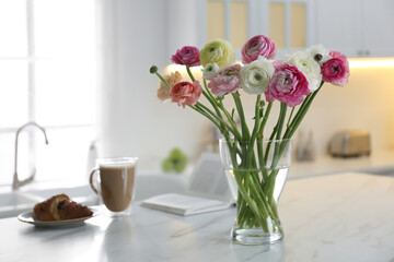 Fototapeta na wymiar Beautiful fresh ranunculus flowers near cup of coffee, croissant and book on table in kitchen