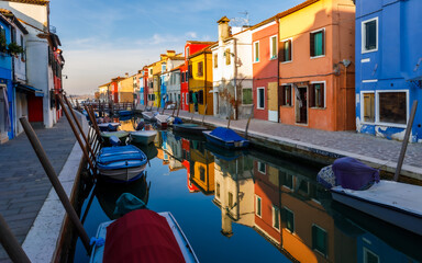 Fototapeta na wymiar Burano island street at sunset with colorful houses, boats and reflections in the water