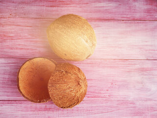 Two coconuts one whole the second is broken on a wooden background
