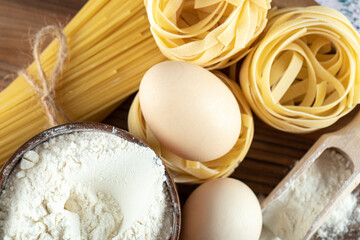 Two types raw pasta with eggs and bowl of flour on wooden board