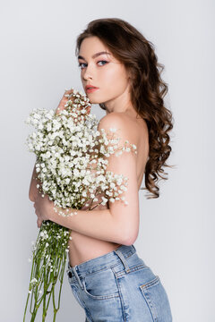 Shirtless Woman In Jeans Holding Small White Flowers Isolated On Grey