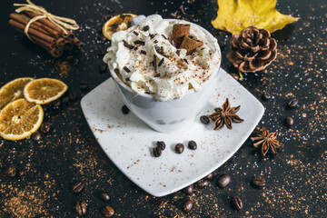 Cup of coffee with cinnamon sticks, whipped cream, chocolate sprinkles and star anise. Cozy winter or autumn hot beverage composition.