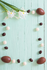 Easter chocolate eggs and flowers on green wooden background