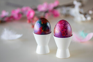 Easter concept. Two decorative eggs in white poached stands and branches of blossoming sakura on a light background.