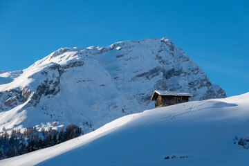 old wooden barn on a snowy slope in front of mountain und blue sky