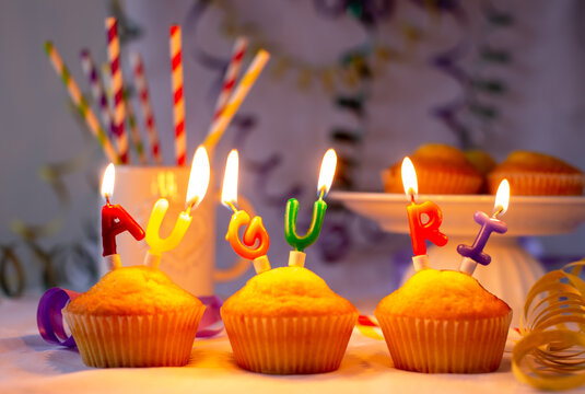 Muffin con candeline colorate accese con la scritta AUGURI su un tavolo imbandito con stelle filanti e cannucce