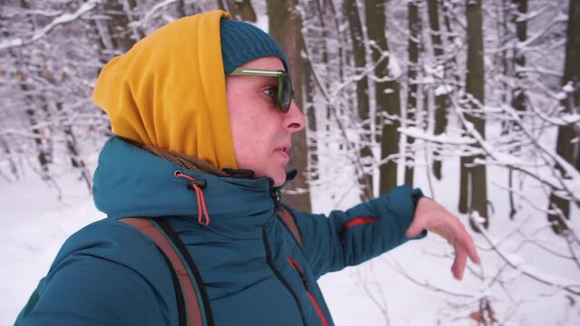 A blogger with glasses tells subscribers the route in the winter forest, he speaks, gestures. Transmission of information over a distance using video hosting.