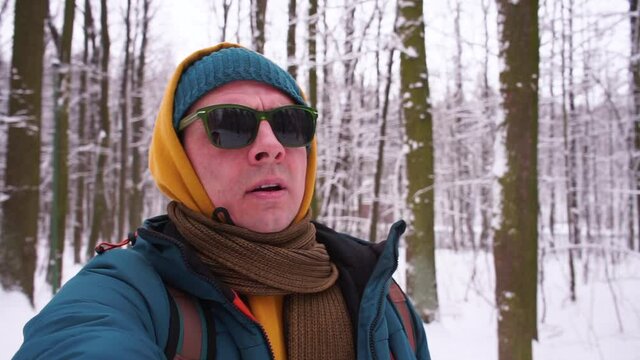 A man with glasses stands in the winter forest. Breathes fresh air. Self-isolation in an open space. Snow lies in the trees. Camera movement.