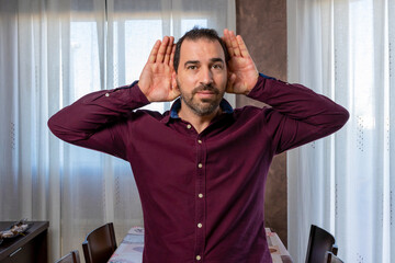 Bearded man in a purple shirt with his hands on his head