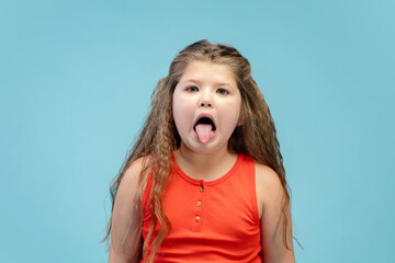 Gremaces. Happy, smiley little caucasian girl isolated on blue studio background with copyspace for ad. Looks happy, cheerful. Childhood, education, human emotions, facial expression concept.
