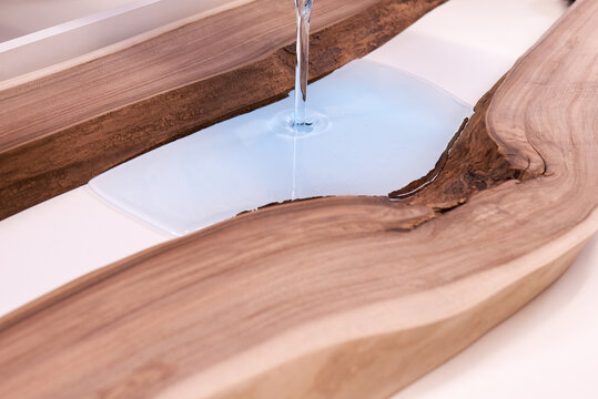 Process making of a craft resin and wood table. Liquid epoxy is poured into a mold with wooden blanks.