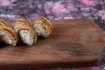 Hot fried sushi rolls with mixed ingredients and crispy cover on a wooden board
