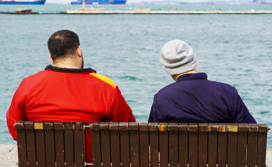 Two men are sitting on a bench in the cold weather  in Konak, in Izmir, in Turkey on February 15, 2021