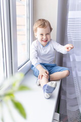 a child boy looks out of the window sitting on the window sill of the house