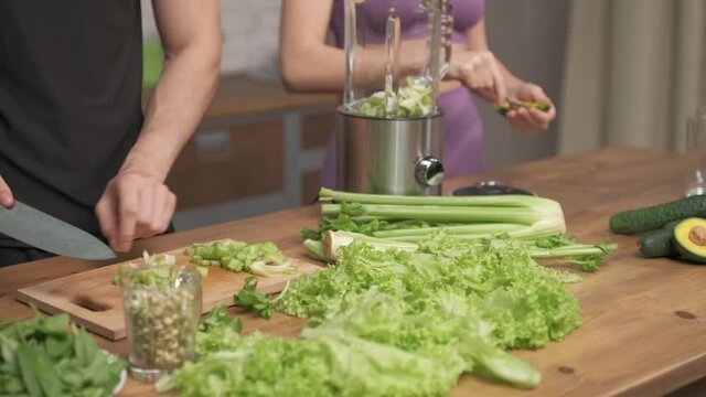 healthy eating, cooking, vegetarian food, dieting and people concept - couple of young peaple with blender and green vegetables making detox shake or smoothie at home. 4 k